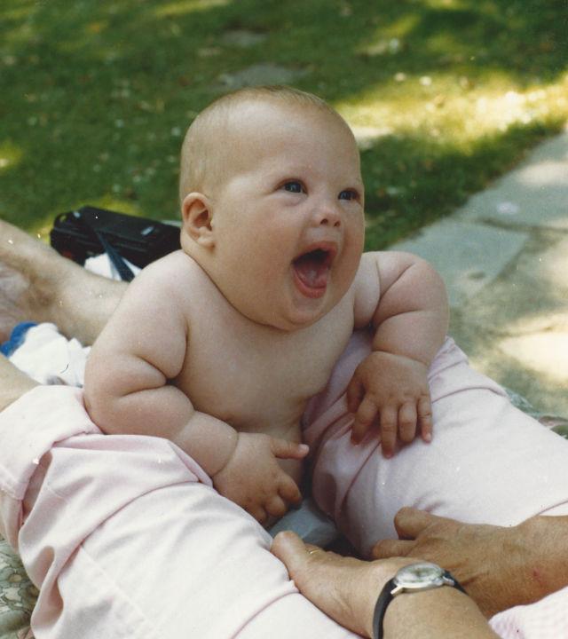 Sam as a baby smiling in someone’s lap.
